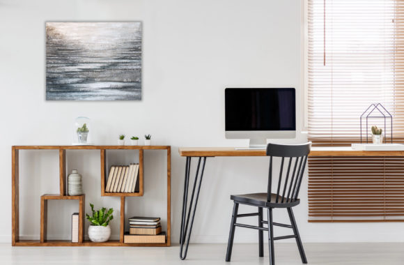 Real photo of a computer with empty screen standing on a wooden desk in bright freelancer's office interior with black chair and bookcase